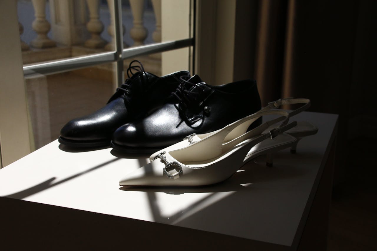Close-up of stylish black mens and white womens shoes in sunlight by a window.