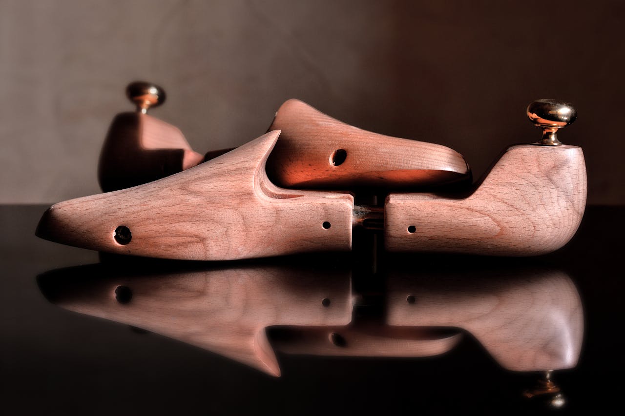 Close-up of polished wooden shoe trees reflecting on a glossy surface, showcasing craftsmanship.